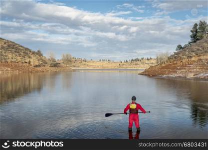 stand up paddler dressed in a drysuit for cold season paddling on a shore of mountain lake in Colorado (Horsetooth Reservoir near Fort Collins)