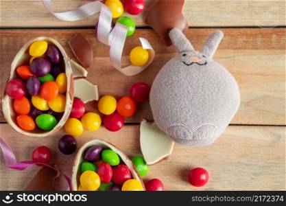 Standard toy easter bunny and chocolate eggs on a brown wooden background.. Standard toy easter bunny and chocolate eggs on a wooden background.