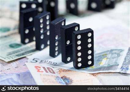 Standing dominoes on pound, euro and dollar bank notes illustrating banking crisis