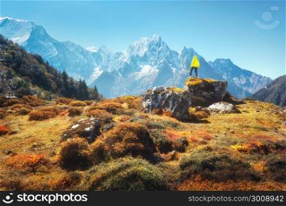 Standing man on the stone and looking on amazing Himalayan mountains. Landscape with traveler, high rocks with snowy peaks, plants, forest in autumn in Nepal. Lifestyle, travel. Trekking in Himalayas