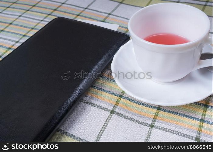 Standing on the table white Cup of tea and a black folder with the receipt for payment. Cup of tea and a black folder with the bill for payment