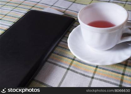 Standing on the table white Cup of tea and a black folder with the receipt for payment. Cup of tea and a black folder with the bill for payment