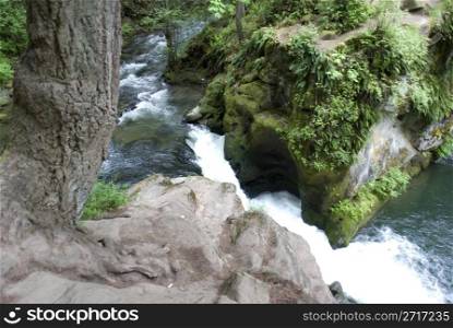 Standing over a cliff overlooking a waterfall consisting of water splashing over many strong boulders in the peaceful forest