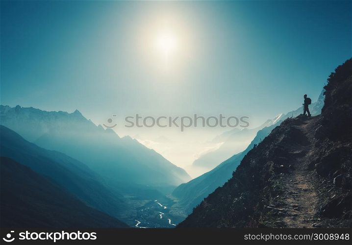 Standing woman on the hill against mountain valley at bright sunny day. Landscape with girl, trail, mountain, blue sky with sun and low clouds at sunset in Nepal. Lifestyle, travel. Trekking