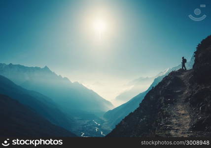 Standing woman on the hill against mountain valley at bright sunny day. Landscape with girl, trail, mountain, blue sky with sun and low clouds at sunset in Nepal. Lifestyle, travel. Trekking