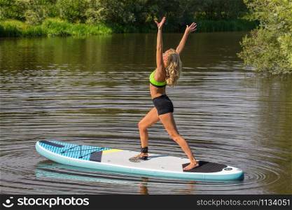 Standing young caucasian woman on SUP in yoga pose on water