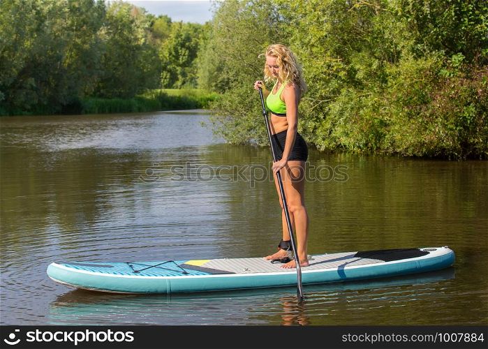 Standing young caucasian woman paddles with SUP on water of river