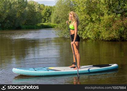 Standing young caucasian woman paddles with SUP on water of river