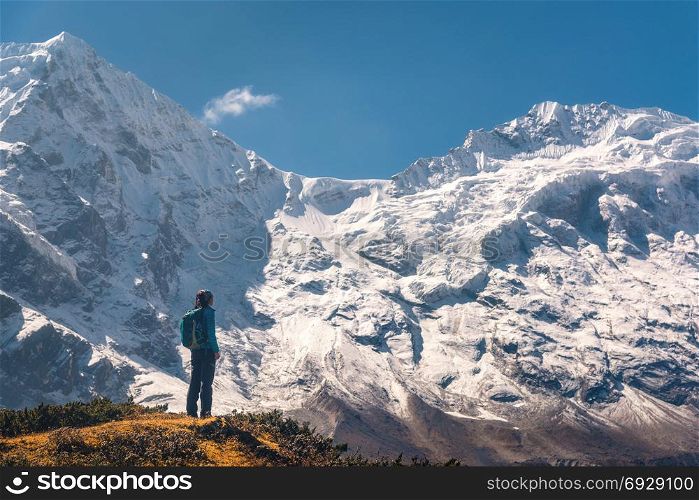 Standing young woman on the hill and looking on amazing Himalayan mountains. Landscape with traveler, high rocks with snowy peaks, blue sky in autumn in Nepal. Lifestyle, travel. Trekking in Himalayas