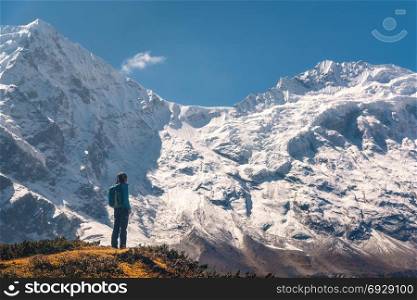 Standing young woman on the hill and looking on amazing Himalayan mountains. Landscape with traveler, high rocks with snowy peaks, blue sky in autumn in Nepal. Lifestyle, travel. Trekking in Himalayas