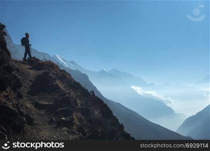 Standing young woman on the hill and looking on mountain valley. Landscape with sporty girl, path, mountain, blue sky with low clouds at sunrise in Nepal. Lifestyle, travel. Trekking in Himalayas