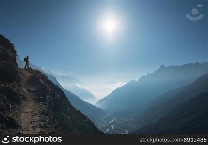 Standing young woman on the hill and looking on mountain valley. Landscape with girl, path, mountain, blue sky with sun and low clouds at sunrise in Nepal. Lifestyle, travel. Trekking in Himalayas. . Standing young woman on the hill and looking on mountains