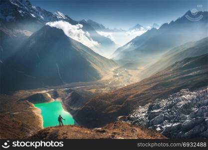 Standing young woman on the mountain peak and looking on beautiful mountain valley with lake, river and hills at sunset. Landscape with girl, rocks in clouds, sky, glacier in Nepal. Travel. Trekking. Young womanand beautiful mountain valley