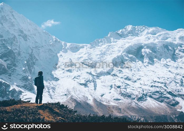 Standing young woman on the mountain trail and looking on snow covered rocks at sunset. Landscape with girl, high mountains with snowy peaks, path, blue sky in Nepal. Travel. Vintage style. Nature
