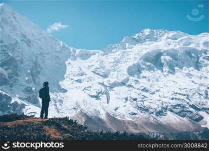Standing young woman on the mountain trail and looking on snow covered rocks at sunset. Landscape with girl, high mountains with snowy peaks, path, blue sky in Nepal. Travel. Vintage style. Nature
