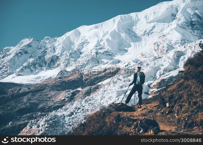 Standing young woman with backpack on the mountain peak and looking on beautiful mountains and glacier at sunset. Landscape with girl, rocks with snowy peaks,blue sky in Nepal.Hiking, travel. Vintage