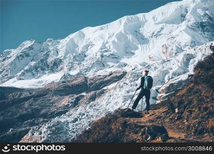 Standing young woman with backpack on the mountain peak and looking on beautiful mountains and glacier at sunset. Landscape with girl, rocks with snowy peaks,blue sky in Nepal.Hiking, travel. Vintage