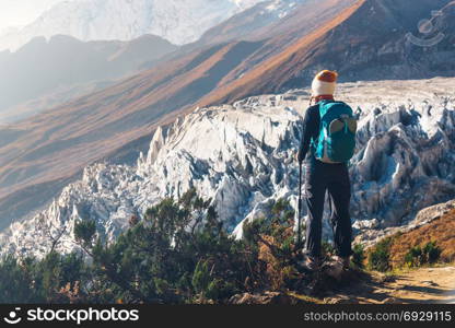 Standing young woman with backpack on the mountain peak and looking on beautiful mountains and glacier at sunset. Landscape with girl, rocks with snowy peaks,blue sky in Nepal.Hiking, travel.Trekking