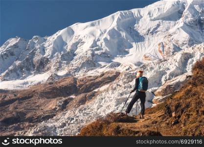 Standing young woman with backpack on the mountain peak and looking on beautiful mountains and glacier at sunset. Landscape with girl, rocks with snowy peaks,blue sky in Nepal.Hiking, travel.Trekking