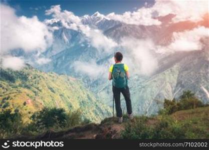 Standing young woman with backpack on the mountain peak in summer. Landscape with girl, beautiful mountain canyon in low clouds, forest with green trees at sunset. Himalayas in Nepal. Travel. Trekking