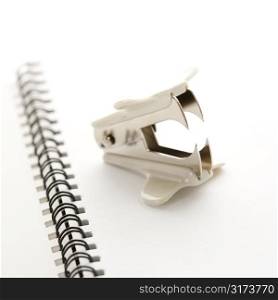 Staple remover on top of an open spiral bound notebook.