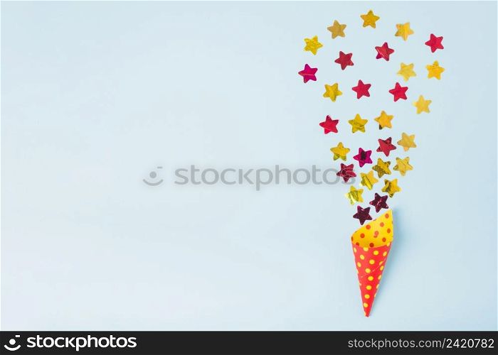 star shape confetti coming out from paper cone with polka dot blue background