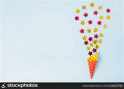 star shape confetti coming out from paper cone with polka dot blue background
