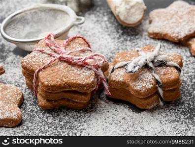 Star shaped baked gingerbread cookies sprinkled with powdered sugar on a black table, close up