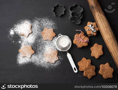 Star shaped baked gingerbread cookies sprinkled with powdered sugar on a black table, top view