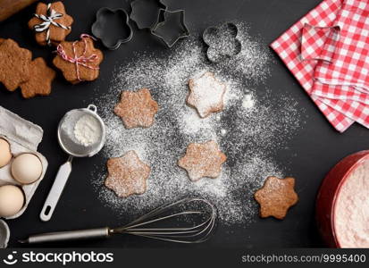 Star shaped baked gingerbread cookies sprinkled with powdered sugar on a black table, top view