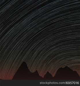 Star trails and far rocks. Abstract background with star trails in the night sky and rocks silhouettes.