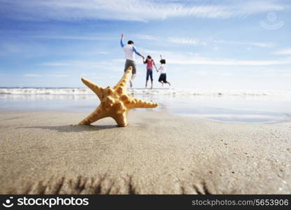 Starfish In Foreground As Father Plays With Children In Sea