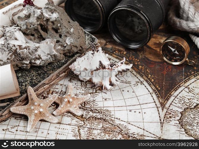 Starfishes, shells, mineral zeolite specimen, compass, old binoculars, rope and scrolls of paper on a background the ancient map; toned image