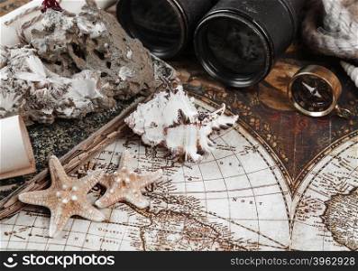Starfishes, shells, mineral zeolite specimen, compass, old binoculars, rope and scrolls of paper on a background the ancient map; toned image