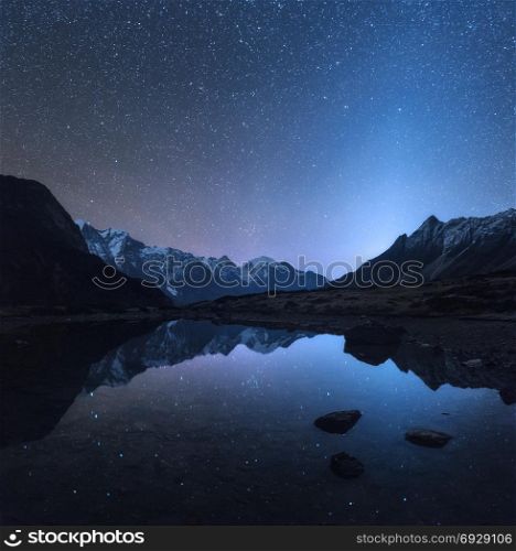 Starry night in Nepal. Amazing night scene with mountains and lake. Landscape with high rocks with snowy peak and sky with stars reflected in water in Nepal. Travel in Himalayas. Space background