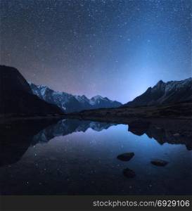 Starry night in Nepal. Amazing night scene with mountains and lake. Landscape with high rocks with snowy peak and sky with stars reflected in water in Nepal. Travel in Himalayas. Space background