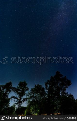 Starry night over the trees near by the city of Kiev in Ukraine. The Milky Way appears in the sky. Cars passes on the road