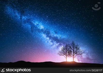 Starry sky with pink Milky Way and trees. Night landscape with alone trees on the hill against colorful milky way. Amazing galaxy. Nature background with beautiful universe. Astrophotography