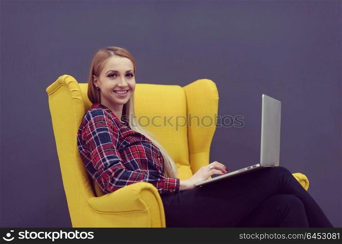 startup business, woman working on laptop computer at modern office and sitting on creative yellow armchair