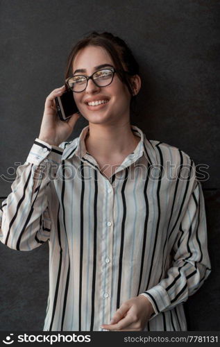 Startup businesswoman in shirt with a glasses using smartphone while standing in front of gray wall during a break from work outside. High-quality photo. Startup businesswoman in shirt with a glasses using smartphone while standing in front of gray wall during break from work outside