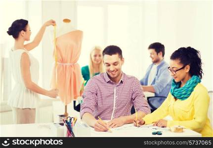 startup, education, fashion and office concept - smiling designers drawing sketches and adjusting dress on mannequin in office