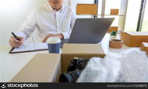 Startup small business entrepreneur SME, young asian man working with laptop computer and delivery packaging box, online market packing, SME e-commerce seller concept