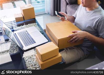 Startup small business SME, entrepreneur owner using smartphone or note book taking receive and checking online purchase shopping order to preparing pack product box