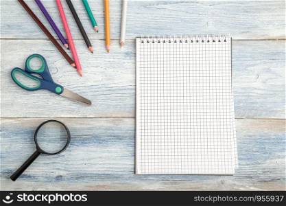 stationery, a paper notebook and a magnifying glass on a light blue old wooden background. top view. flat lay