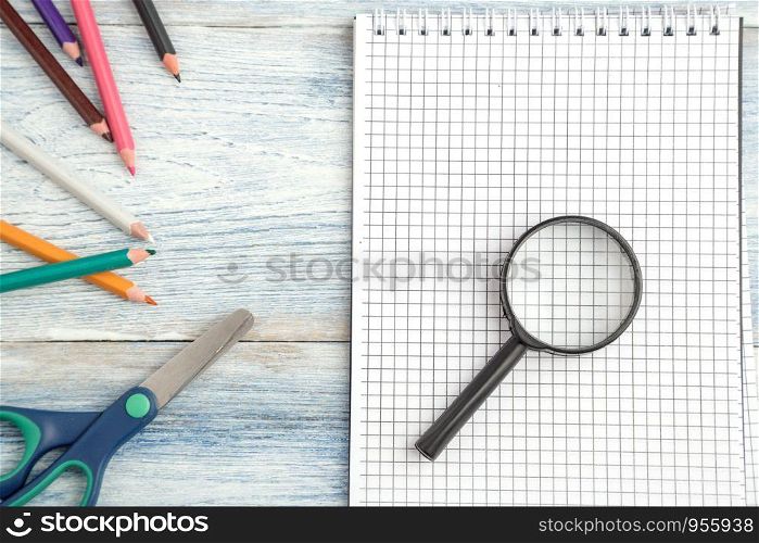 stationery, a paper notebook and a magnifying glass on a light blue old wooden background. top view. flat lay