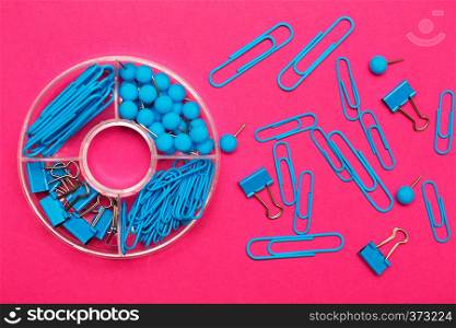 stationery paper clips, binders and buttons in blue on pink background