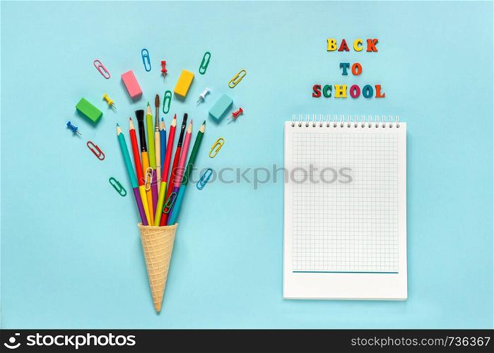 Stationery Pencils paintbrush paperclip in waffle ice cream cone and notepad. Text Back To School Still life on blue background. Mockup Copy space Flat lay Top view Concept Education. Stationery Pencils paintbrush paperclip in waffle ice cream cone