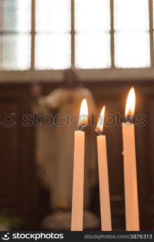 Statue of Jesus Christ in Church with Lit Burning Candles in Foreground