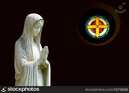 Statue of Mary praying in profile with isolation path and out of focus cross shaped window on the right
