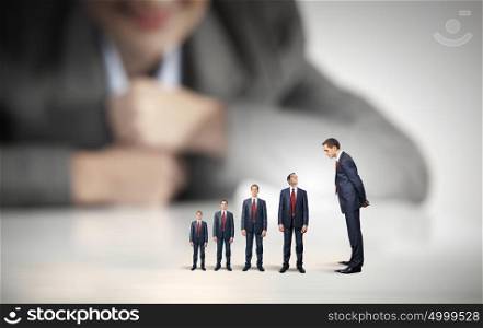 Status in business. Businesswoman looking at miniature of business people of different sizes